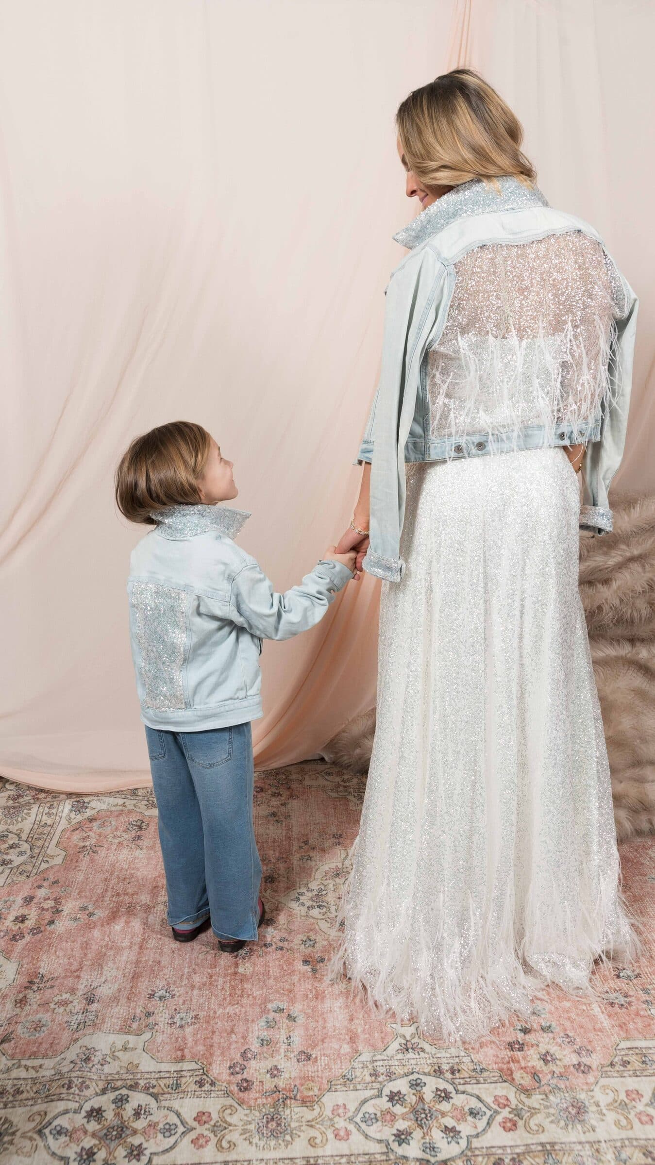 Mother and child hand in hand in matching pale denim jackets, the bride in a beaded gown